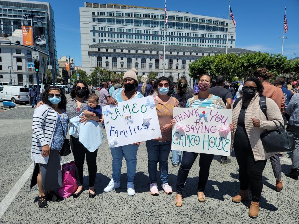 Six women stand in front of San Francisco City Hall with signs saying "Cameo Families" and "Thank You for Saving Cameo House".